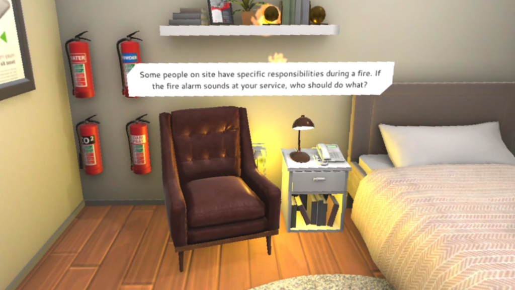 A VR bedroom scene with a bed, bedside table and lamp, armchair and four fire extinguishers with the text 'Some people on site have specific responsibilities during a fire. If the fire alarm sounds at your service, who should do what?'