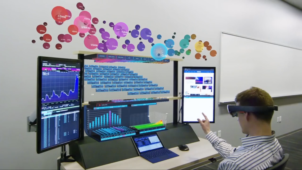 person wearing VR goggles seated in front of several computer screens , that display graphics and data visualisations, person controls screens with the movement of his hand