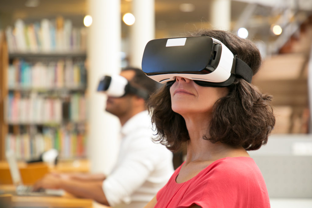 Close up of a woman and man using VR headsets in a library, the woman is in the foreground in focus
