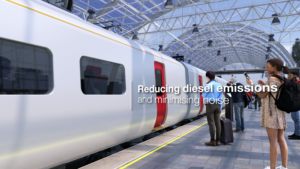 Battery powered train in station with people on platform, woman with rucksack texting