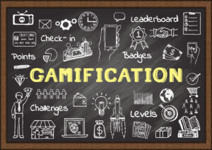 A chalkboard-style illustration featuring various icons and elements related to gamification. The central focus is the word 'Gamification' written in bold yellow letters.