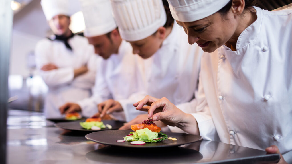 Professional chefs plating food in a commercial kitchen, focusing on presentation and precision during culinary training. VR training for hospitality.