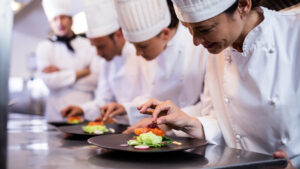 Professional chefs plating food in a commercial kitchen, focusing on presentation and precision during culinary training. VR training for hospitality.